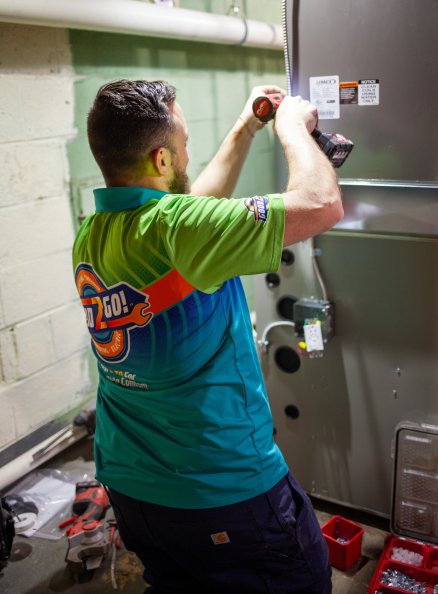 An HVAC technician from Good2Go uses a power drill to perform maintenance or repairs on a Lennox furnace unit in a basement utility room, surrounded by tools and equipment.